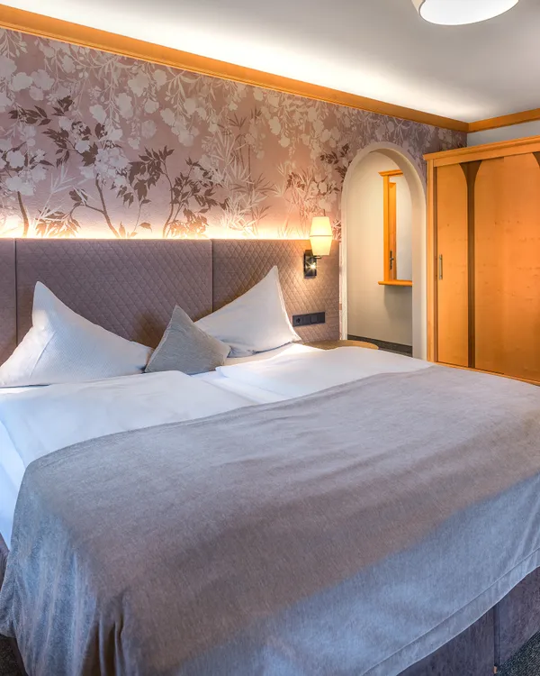 Gemütliches Hotelzimmer mit Doppelbett, Blumenwand und Kleiderschrank aus Holz